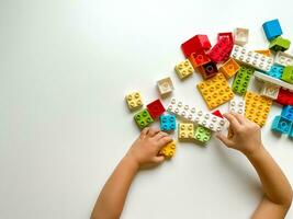 Child plays with colorful building blocks on white background. Empty space for text. View from above photo