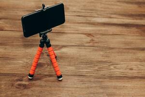 The phone stands on a manual monopod tripod for the camera on a wooden table.. photo