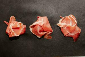 Pieces of dried pork jamon prosciutto on a black board photo