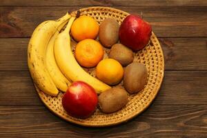 Fruit banana, kiwi, apple, tangerines lie in a wicker plate. photo