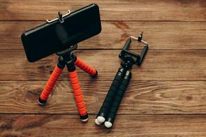 The phone stands on a manual monopod tripod for the camera on a wooden table.. photo
