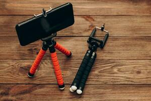 The phone stands on a manual monopod tripod for the camera on a wooden table.. photo