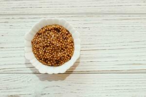 grain mustard in a white bowl on a white table. photo
