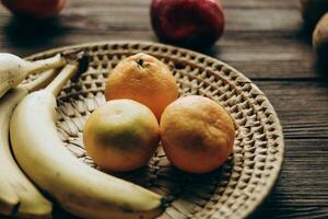 A wicker bowl with fruit stands on a wooden brown table. photo