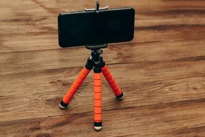 The phone stands on a manual monopod tripod for the camera on a wooden table.. photo