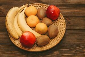 Fruit banana, kiwi, apple, tangerines lie in a wicker plate photo