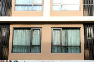 Glass window with window tint and black painted aluminium frame on light wall of building, sunlight on wall and curtain behind window. photo