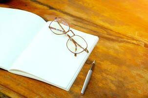 open notebook with glasses and pen on wooden table photo