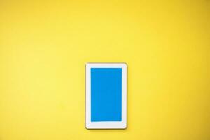 un blanco tableta con un azul pantalla en un amarillo antecedentes foto