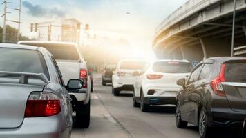 Rear side of car on the road with many cars queue up from the traffic lights. Beside with bridge made from cement. Background of bright orange and sky. photo