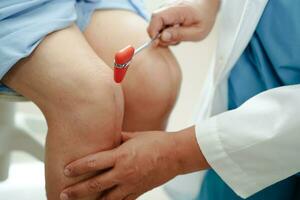 Asian doctor knock on knee reflex nerve for check and treatment senior patient in hospital. photo