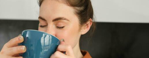 cerca arriba retrato de hermoso, relajado joven mujer, disfrutando aroma de café, Bebiendo capuchino y sonriente foto