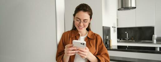 Beautiful woman checking social media while using smartphone at home. Smiling young female using mobile phone app and playing game, shopping online or reading news. Copy space photo