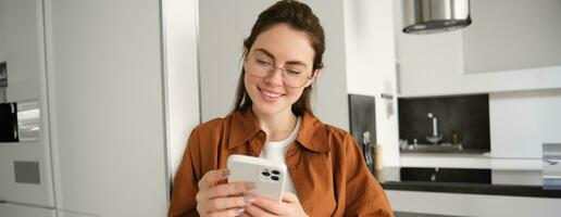 Beautiful woman checking social media while using smartphone at home. Smiling young female using mobile phone app and playing game, shopping online or reading news. Copy space photo