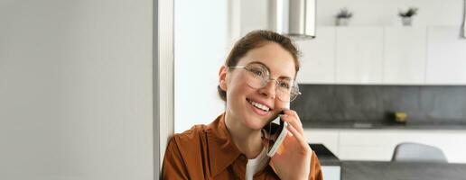 Portrait of happy smiling young woman at home, talking on mobile phone, calling friend and having nice conversation, answer telephone photo