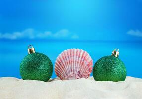 Pink conch with Christmas shiny green balls on sand of beach with sea. New Year, holiday. Copy space photo