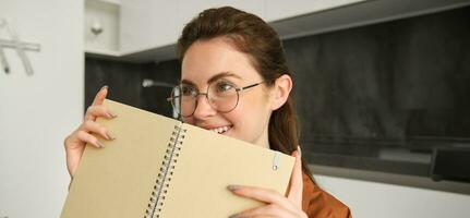 Portrait of beautiful young woman studying, student revising at home, doing homework, holding planner, reading her notes and smiling, writing in diary photo