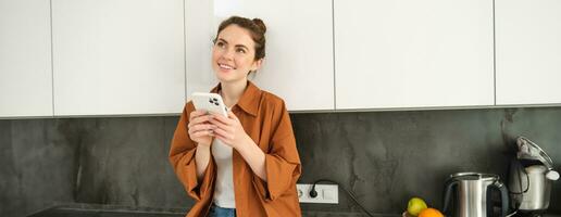 Image of young woman with smartphone, looking with thoughtful expression, buying online using mobile app, orders food delivery with phone application photo