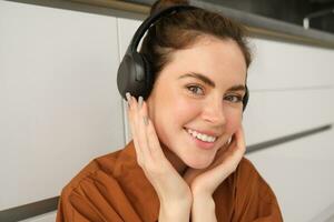 Close up shot of modern stylish woman in headphones, relaxes while listens to music in wireless earphones photo