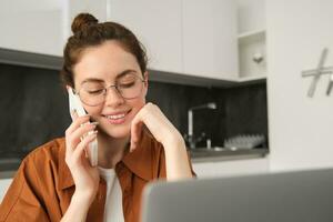 Portrait of young woman at home, doing online shopping. Businesswoman has own startup making a phone call, has conversation with client, saleswoman trading online, using laptop photo