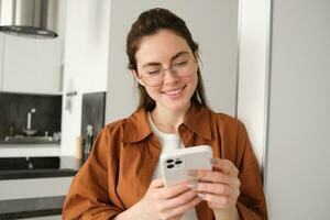 hermosa mujer comprobación social medios de comunicación mientras utilizando teléfono inteligente a hogar. sonriente joven hembra utilizando móvil teléfono aplicación y jugando juego, compras en línea o leyendo noticias. Copiar espacio foto