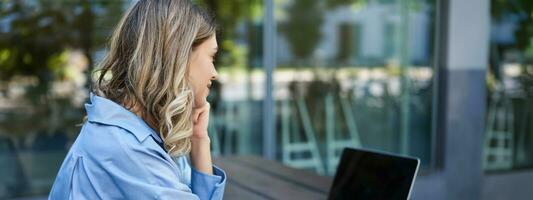 Close up portrait of woman student attend online course classes, sitting outside on fresh air with laptop and taking notes. Businesswoman video chat on computer photo