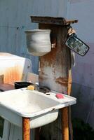 Homemade corner for washing hands and dishes in the garden of a village house - an old metal washbasin and sink with sponges, a mirror and brushes for the summer season in Russia. Vertical photo