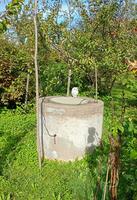 A round stone well for extracting water in the garden on a sunny autumn day. Vertical photo, general plan photo