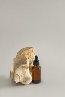 Amber Glass Cosmetic Bottle with Dropper with Serum or Cosmetic Skin Care Oil on Grey Background with Natural Stone. Vertical view. photo