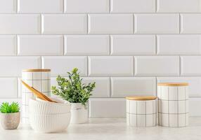 Set of stylish white ceramic jars with bamboo lids and white ceramic bowls on white stone countertop. Trendy eco style in a modern kitchen. photo