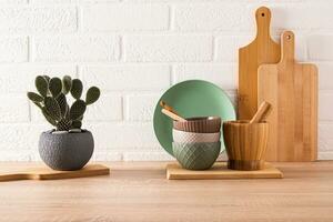 Set of ceramic bowls and cutting boards on wooden light countertop in modern kitchen with potted opuntia, cactus. Front view. minimalism. photo