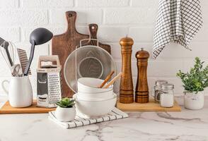 different kitchen utensils and tools made of natural materials on a light stone countertop and plants in pots front view. Eco-friendly cuisine. photo