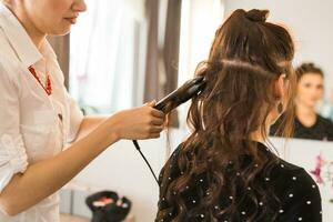 Close up of stylist's hand using curling iron for hair curls. photo