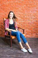 Cute woman with long legs sitting in the armchair behind a brick wall photo