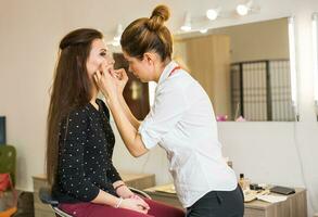 Makeup artist doing make-up for young beautiful woman photo