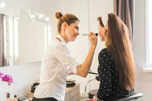 Makeup artist doing make-up for young beautiful woman photo