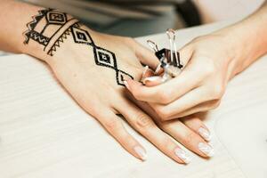 young woman mehendi artist painting henna on the hand photo