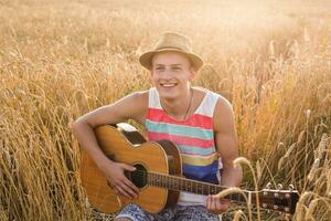 Cheerful traveling musician with his guitar outside in a wheat field. photo