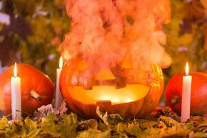 Halloween pumpkin lantern with dry leaves, candles and smoke photo