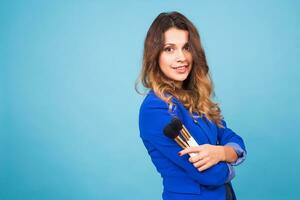 Young make-up artist with brushes on blue background photo