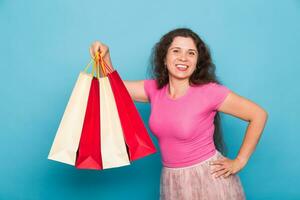 Portrait of young happy smiling woman with shopping bags, over blue background. Purchase, sale and people concept photo