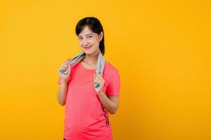 Portrait young asian sports fitness woman happy smile wearing pink sportswear and face towel doing exercise training workout against yellow studio background. wellbeing and healthy lifestyle concept. photo