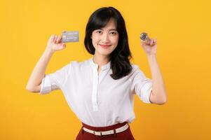 Portrait beautiful young asian woman enterpriser happy smile wearing white shirt and red plants holding credit card and crypto digital currency isolation on yellow background. Wealth concept. photo