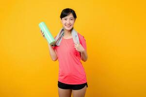 Portrait young asian sports fitness woman happy smile wearing pink sportswear and face towel doing exercise training workout against yellow studio background. wellbeing and healthy lifestyle concept. photo