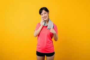 retrato joven asiático Deportes aptitud mujer contento sonrisa vistiendo rosado ropa de deporte y cara toalla haciendo ejercicio formación rutina de ejercicio en contra amarillo estudio antecedentes. bienestar y sano estilo de vida concepto. foto