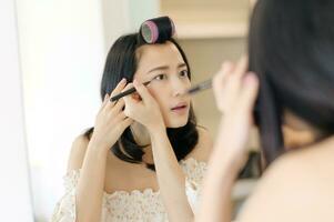 Beautiful young Asian woman applying makeup in front of the mirror. Lifestyle people concept. Advertisement for skin cream, anti-wrinkle cream, baby face photo