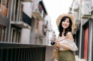 Happy youth asian woman with camera travels street city trip on leisure weekend. Young hipster female tourist sightseeing summer urban Bangkok destination. Asia summer tourism concept. photo