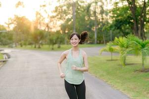 ajuste asiático joven mujer trotar en parque sonriente contento corriendo y disfrutando un sano al aire libre estilo de vida. hembra persona que practica jogging. aptitud corredor niña en público parque. sano estilo de vida y bienestar siendo concepto foto