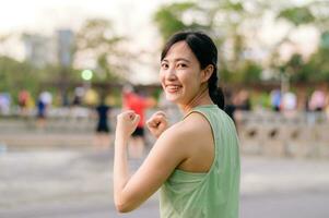 Female jogger. Fit young Asian woman with green sportswear aerobics dance exercise in park and enjoying a healthy outdoor. Fitness runner girl in public park. Wellness being concept photo