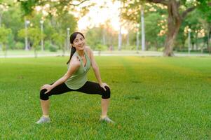 Female jogger. Fit young Asian woman with green sportswear stretching muscle in park before running and enjoying a healthy outdoor. Fitness runner girl in public park. Wellness being concept photo